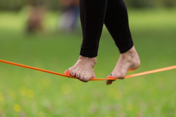 Lady practising slack line in the city park. Slacklining is a practice in balance that typically uses nylon or polyester webbing tensioned between two anchor points.