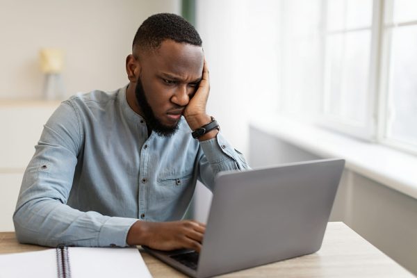 Unhappy Black Businessman Looking At Laptop Hating His Boring Job Sitting At Workplace In Modern Office. Depressed Employee, Burnout At Work. Entrepreneurship And Business Issue And Crisis Concept